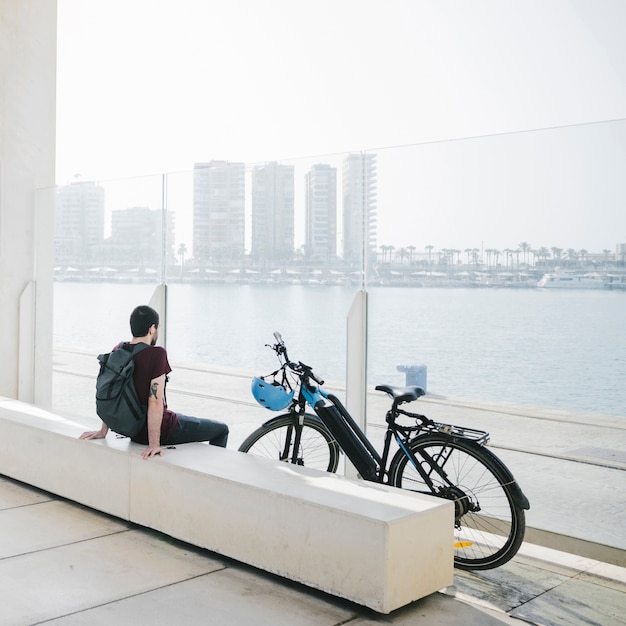 Vista trasera hombre sentado al lado de bicicleta eléctrica