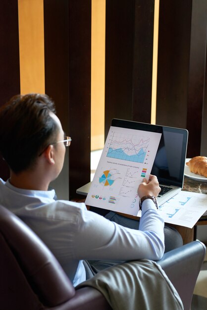 Vista trasera del hombre sentado en el sillón en la cafetería analizando diagramas y gráficos antes de la presentación