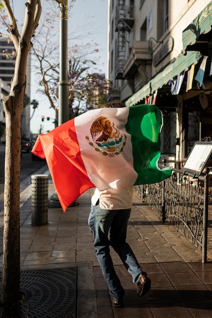 Vista trasera hombre sosteniendo bandera mexicana afuera