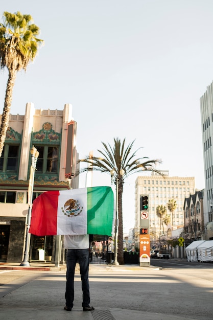 Vista trasera hombre sosteniendo bandera mexicana al aire libre