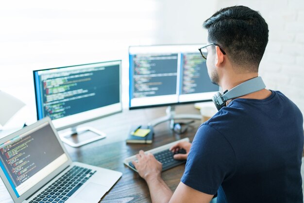 Vista trasera de un joven desarrollador de software latino programando mientras trabaja desde casa