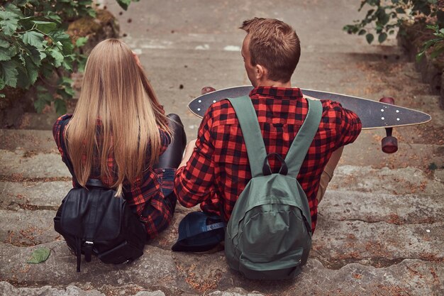 Vista trasera de una joven pareja hipster, sentada en los escalones del parque.