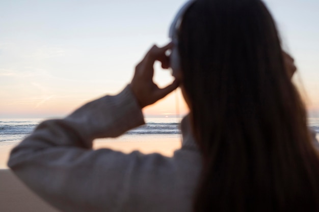 Vista trasera de la mujer con auriculares en la playa