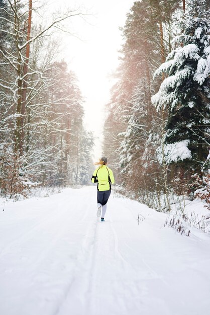 Vista trasera de la mujer corriendo en el bosque de invierno