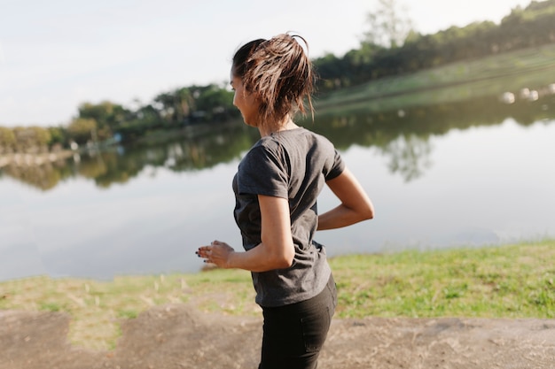 Vista trasera de mujer corriendo junto al lago