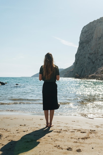 Vista trasera de una mujer joven de pie en la hermosa playa