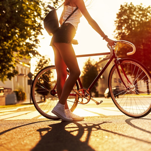 Vista trasera de mujer joven sujetando su bicicleta al atardecer