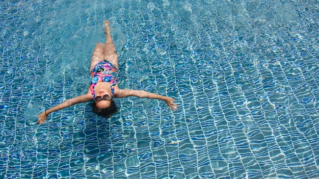 Vista trasera de una mujer nadando en piscina relajante con los brazos abiertos de par en el agua cristalina.