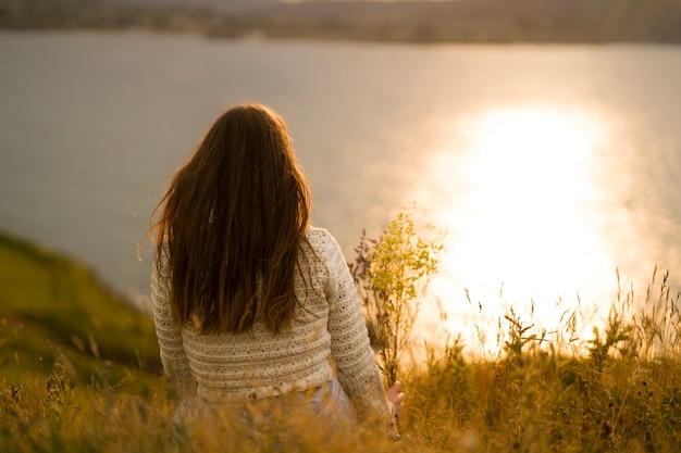 Foto gratuita vista trasera mujer sentada junto al lago