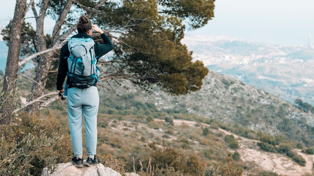 Vista trasera de una mujer con su mochila de pie sobre una roca con vistas a la montaña