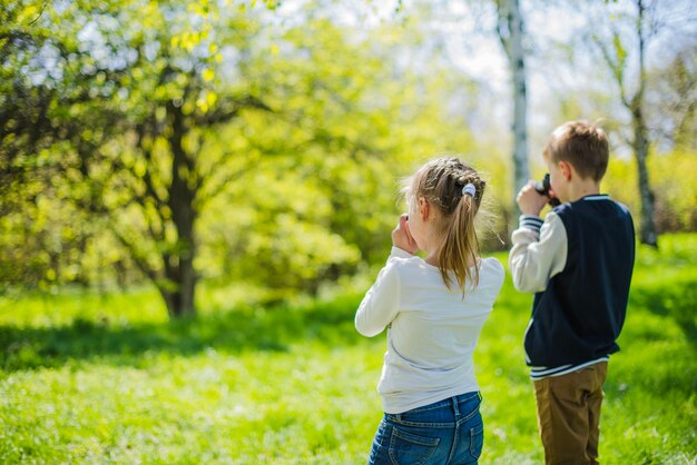 Vista trasera de niña con cámara y chico con prismáticos