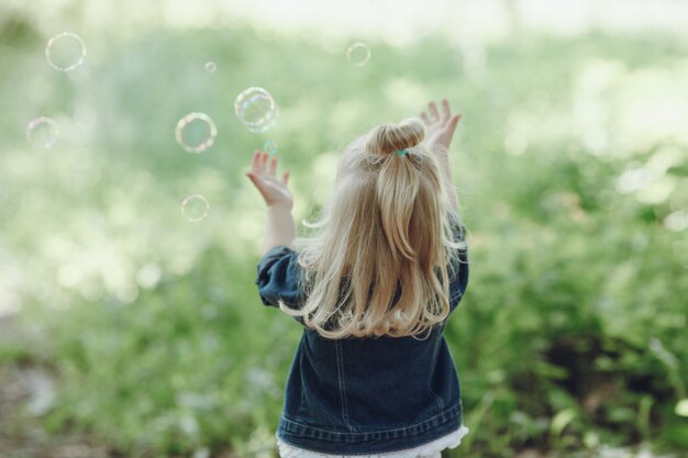 Vista trasera de niña jugando con pompas de jabón