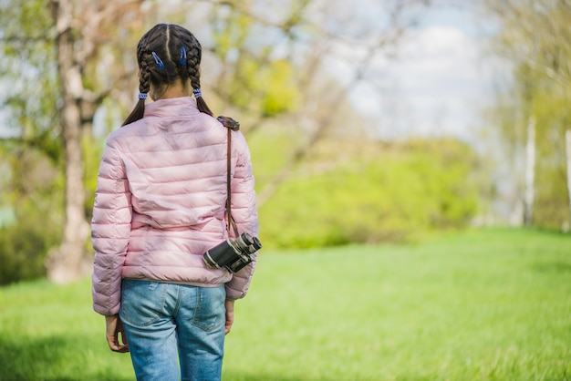 Foto gratuita vista trasera de niña con prismáticos caminando al aire libre