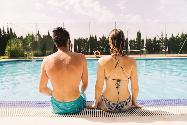 Vista trasera de pareja sentada en borde de piscina