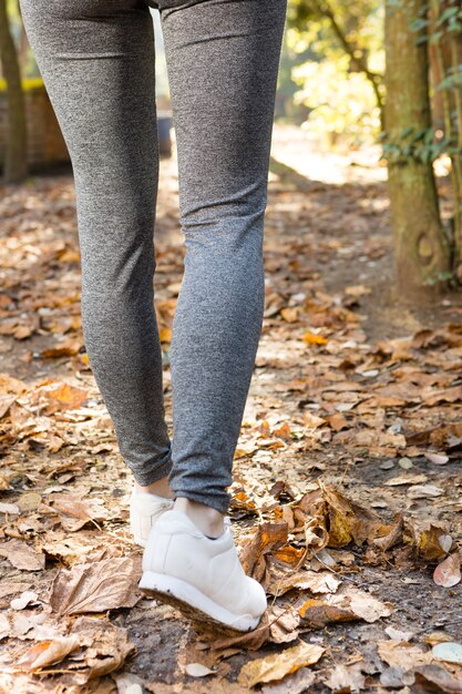 Vista trasera de las piernas de una mujer caminando sobre hojas secas