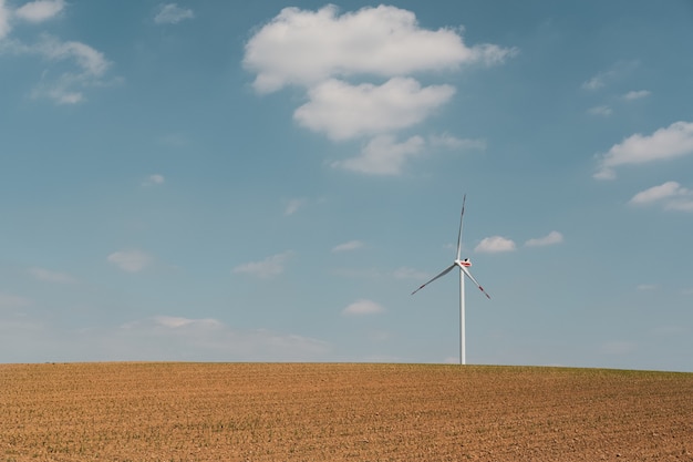 Vista de la turbina eólica y la granja marrón bajo el cielo azul y las nubes blancas