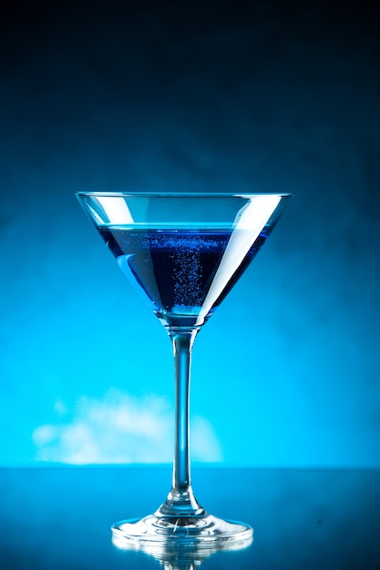 Vista vertical de agua azul en una copa de vidrio sobre fondo oscuro