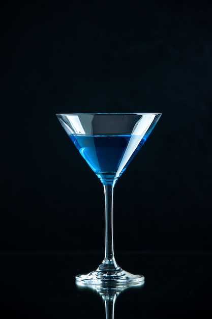 Vista vertical de agua azul en una copa de vidrio sobre fondo oscuro
