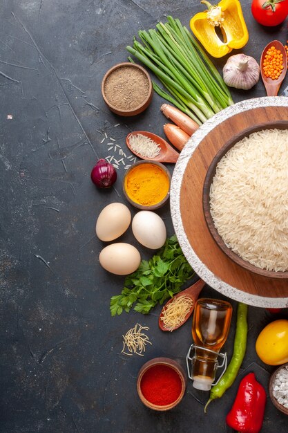 Vista vertical de arroz en una olla marrón sobre una tabla de madera vegetales orgánicos huevos botella de aceite caído pimienta sobre negro