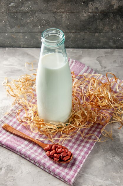 Vista vertical de la botella de vidrio abierta llena de leche y frijoles en una cuchara sobre una toalla despojada de color púrpura