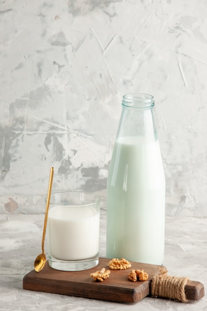 Vista vertical de la botella de vidrio abierta y la taza llena de cuchara de leche y nuez sobre fondo de hielo