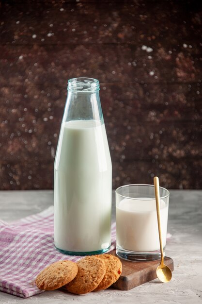 Vista vertical de la botella de vidrio abierta y la taza llena de galletas de leche en una toalla despojada de color púrpura sobre una tabla de cortar de madera