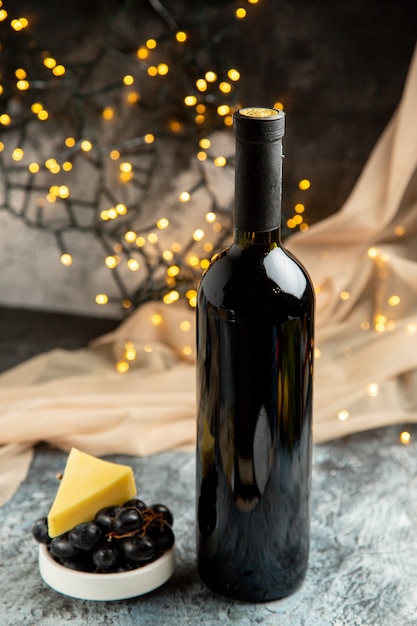 Vista vertical de la botella de vino tinto para la celebración familiar servida con frutas en una olla blanca sobre fondo oscuro