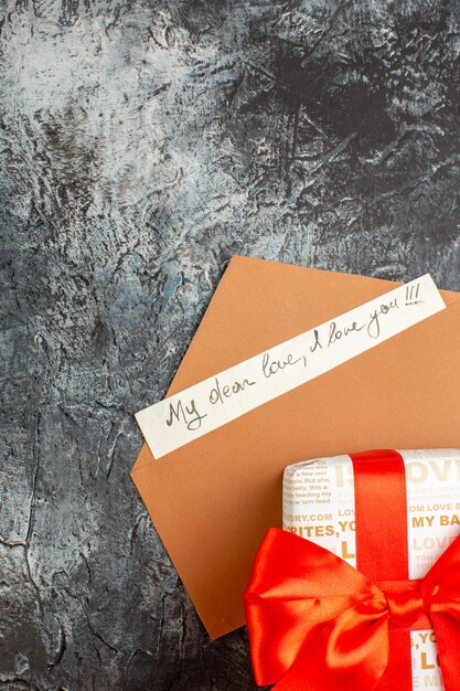 Vista vertical de la caja de regalo bellamente empaquetada atada con una cinta roja en un sobre con una carta de amor sobre un fondo oscuro helado