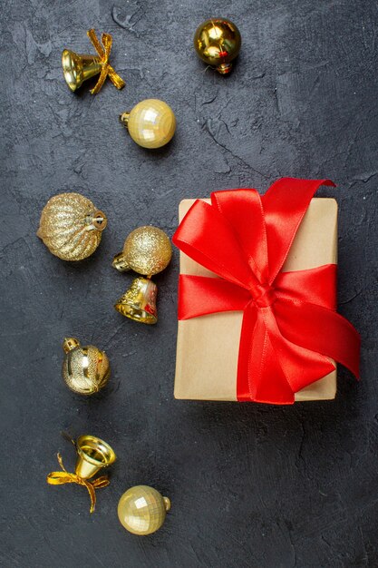 Vista vertical de la caja de regalo con cinta roja y accesorios de decoración en mesa oscura