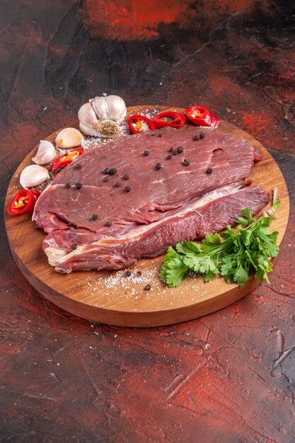 Vista vertical de la carne roja en la bandeja de madera y ajo, limón, cebolla, tenedor y cuchillo sobre fondo oscuro