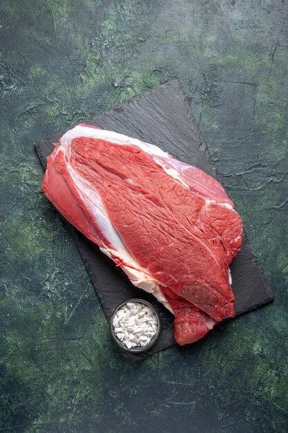 Vista vertical de la carne roja fresca cruda y la sal en la tabla de cortar sobre fondo verde negro mezcla de colores