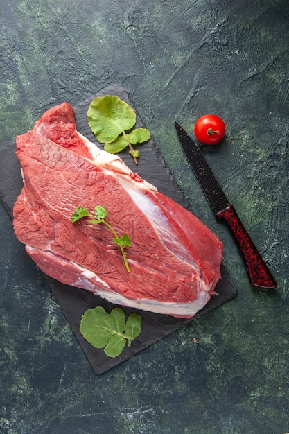 Vista vertical de la carne roja fresca cruda y verduras en la placa de corte de tomate cuchillo sobre fondo verde negro mezcla de colores