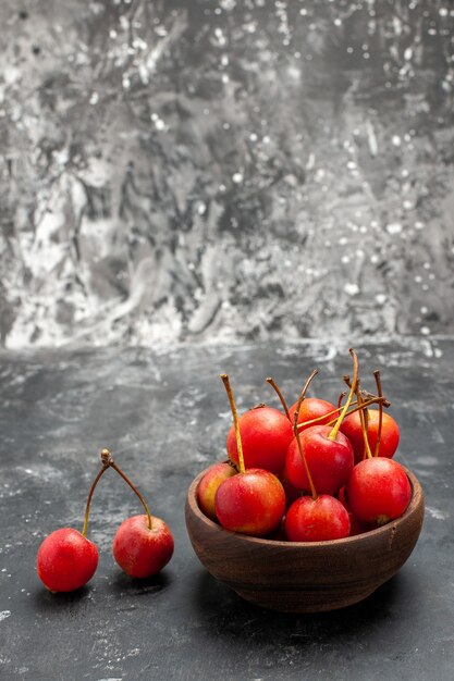 Vista vertical de cereza roja fresca en un recipiente marrón sobre gris