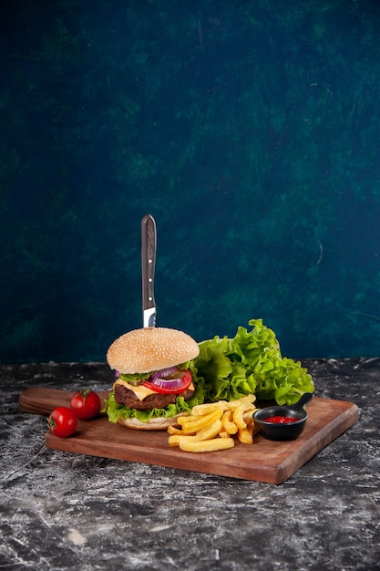 Vista vertical de cuchillo en sándwich de carne y tomates fritos con tallo de pimienta en tablero de madera ketchup sobre superficie azul oscuro