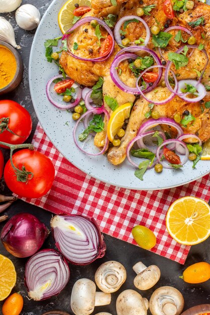 Vista vertical de una deliciosa cena plato de pollo frito con varias especias y alimentos ajos botella de aceite caída limón sobre fondo de color oscuro