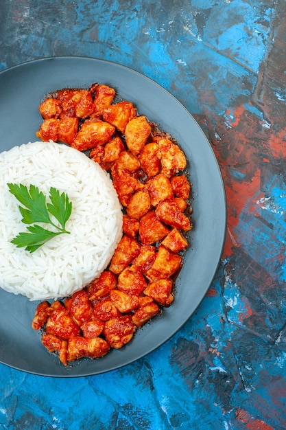 Vista vertical de la deliciosa comida de arroz con pollo verde y tomate sobre fondo azul.