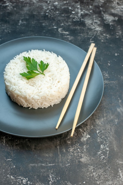 Foto gratuita vista vertical de la deliciosa comida de arroz servida con palillos verdes y sobre una placa negra sobre fondo oscuro