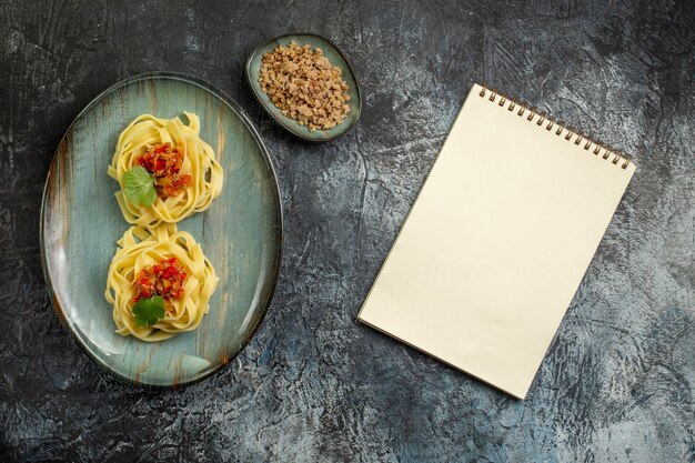 Vista vertical de la deliciosa comida de pasta con carne de tomate y verde sobre una placa azul junto al cuaderno de espiral sobre fondo de hielo