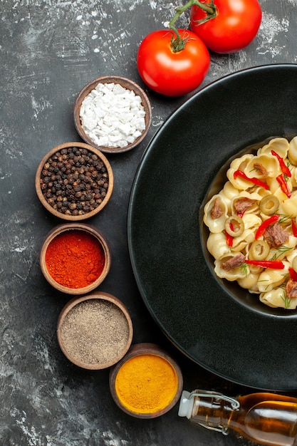 Vista vertical de la deliciosa conchiglie con verduras verdes en un plato y cuchillo y diferentes especias botella de aceite caído sobre mesa gris