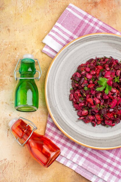 Vista vertical de una deliciosa ensalada con remolacha y frijol y dos botellas de aceite caídas sobre una toalla despojada de color rosa sobre fondo de colores mezclados