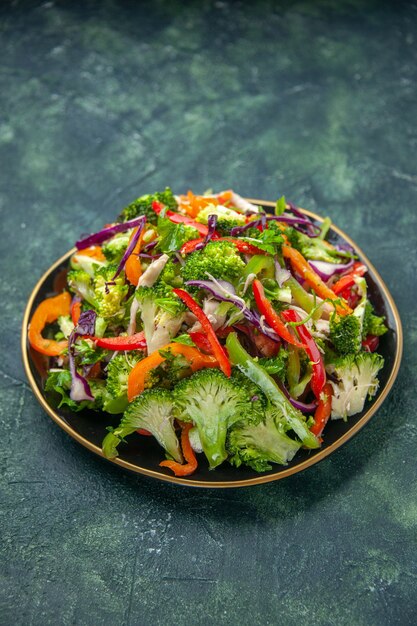 Vista vertical de una deliciosa ensalada vegana en un plato con diversas verduras frescas sobre fondo oscuro