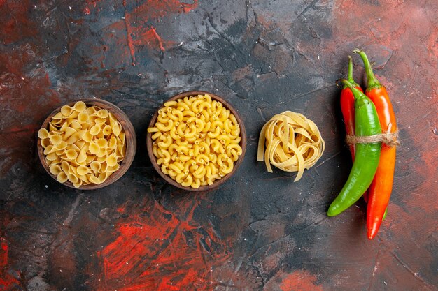 Vista vertical de la deliciosa preparación de la cena con pastas crudas en diversas formas y pimientos atados entre sí sobre fondo de colores mezclados