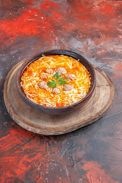 Vista vertical de la deliciosa sopa de fideos con pollo en la tabla de cortar de madera sobre fondo oscuro