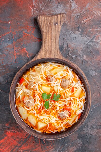 Vista vertical de la deliciosa sopa de fideos con pollo en la tabla de cortar de madera sobre fondo oscuro