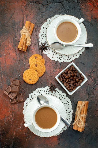 Vista vertical de un delicioso café en tazas blancas galletas canela limas barras de chocolate sobre fondo de colores mezclados