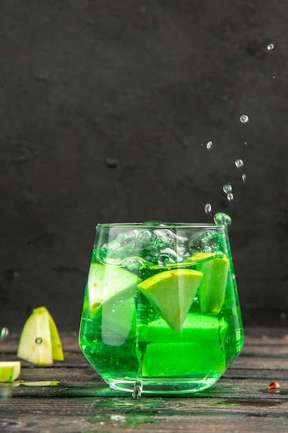 Vista vertical de delicioso jugo natural fresco en un vaso servido con limones de manzana sobre fondo negro