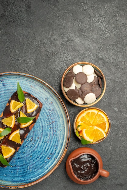Vista vertical de un delicioso pastel decorado con limón y chocolate con otras galletas en la mesa oscura