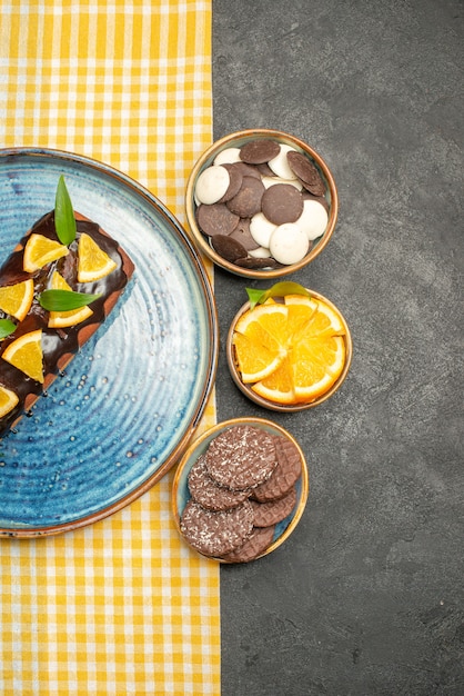 Foto gratuita vista vertical de un delicioso pastel sobre una toalla despojada de amarillo y galletas en el cuadro negro