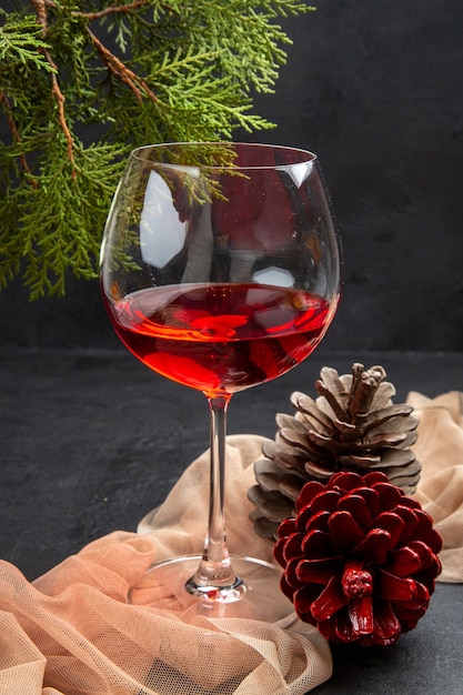 Vista vertical del delicioso vino tinto en una copa de cristal sobre una toalla y ramas de abeto conos de coníferas sobre un fondo oscuro