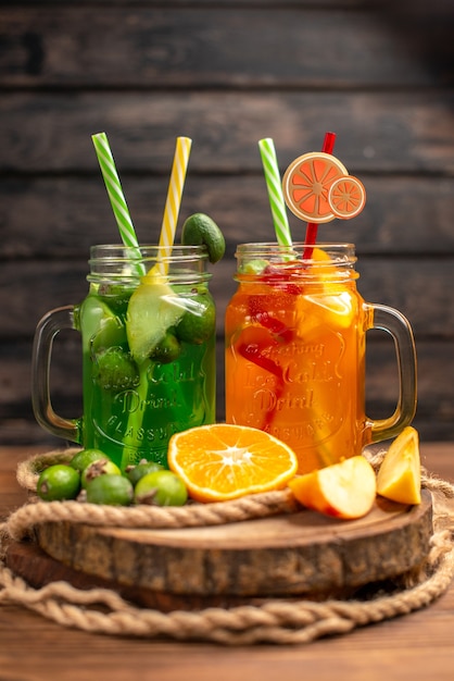 Vista vertical de deliciosos jugos y frutas frescas en una bandeja de madera sobre un fondo marrón